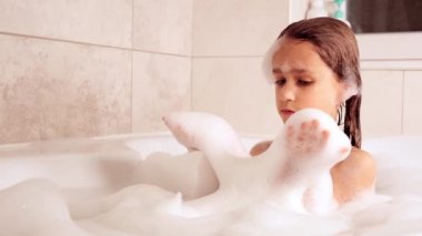 Küçük kız küvette banyo yapıyor ve köpükle oynuyor, hijyen ve bebek bakımı konsepti, 4K UHD hala video kamera, 2x yavaş çekim.