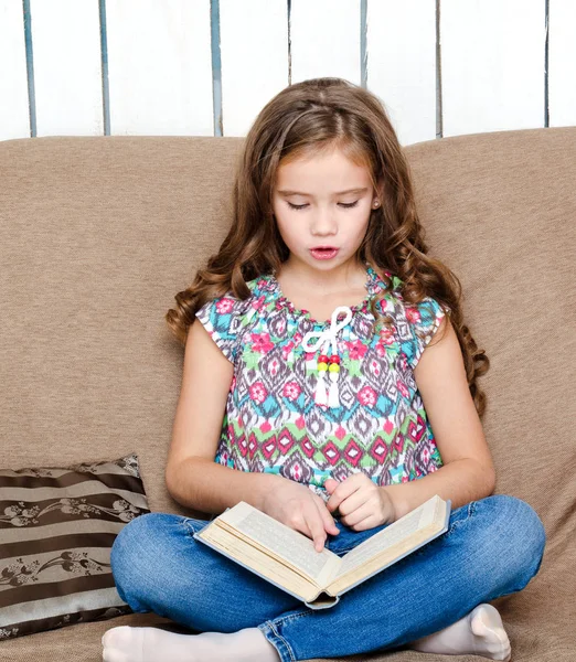 Roztomilá holčička čte knihu na pohovce — Stock fotografie