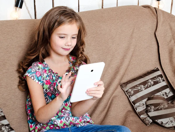 Симпатичная маленькая девочка с планшетным компьютером на диване дома — стоковое фото