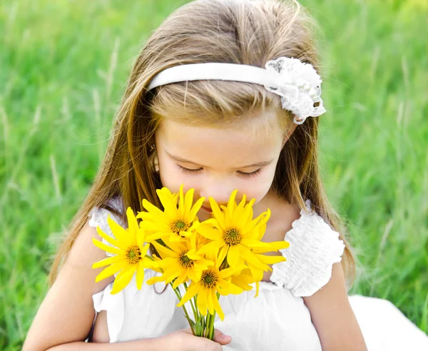 Linda niña oliendo flores en el prado — Foto de Stock
