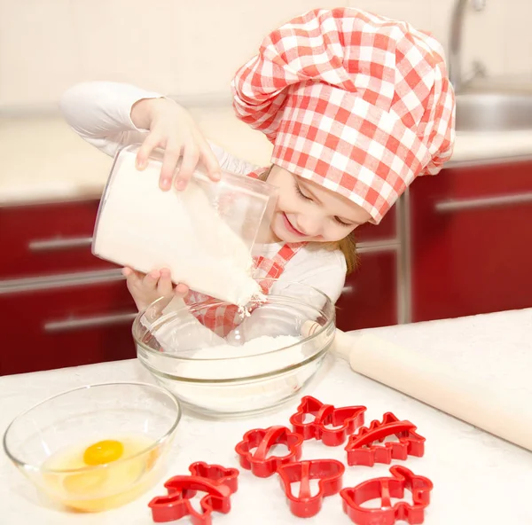 Smiling little girl with chef hat put flour for baking cookies — Stock Photo, Image