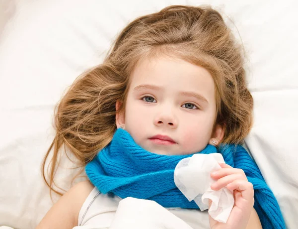 Sick little girl lying in the bed with scarf and tissue — Stock Photo, Image