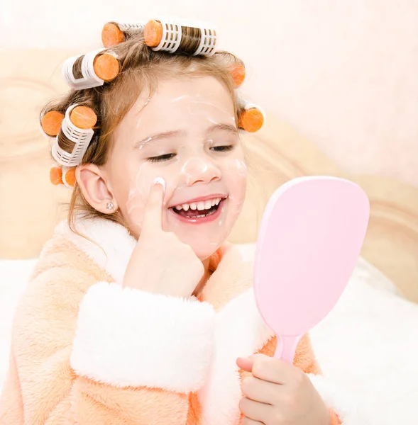 Feliz linda niña en rulos de pelo con espejo aplicando crea — Foto de Stock