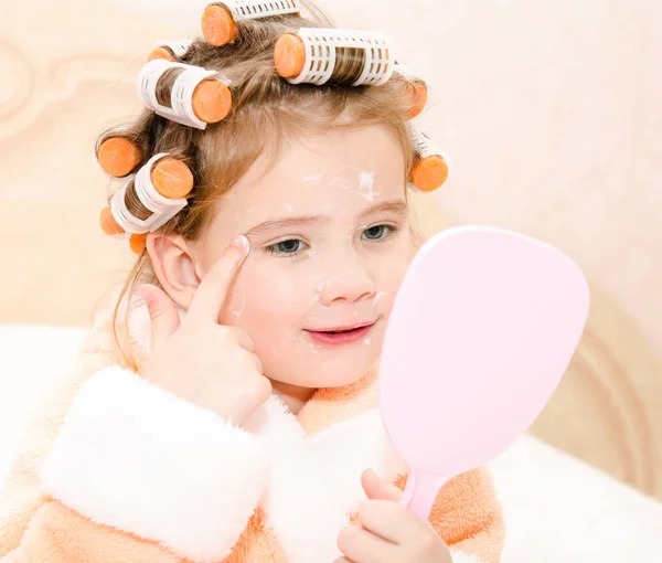 Feliz linda niña en rulos de pelo con espejo aplicando crea — Foto de Stock