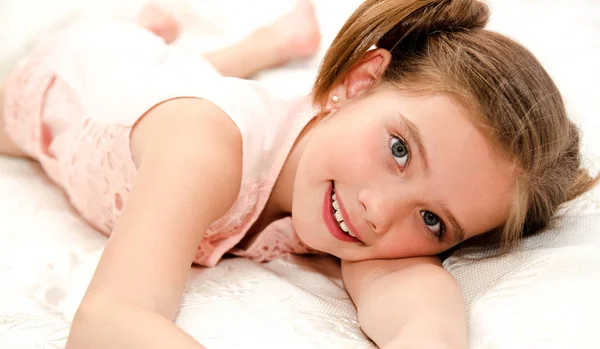 Очаровательная улыбающаяся маленькая девочка отдыхает на кровати. — стоковое фото