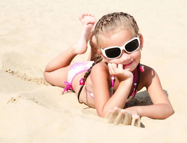 Happy cute little girl in sunglasses lying on the sand — Stock Photo, Image