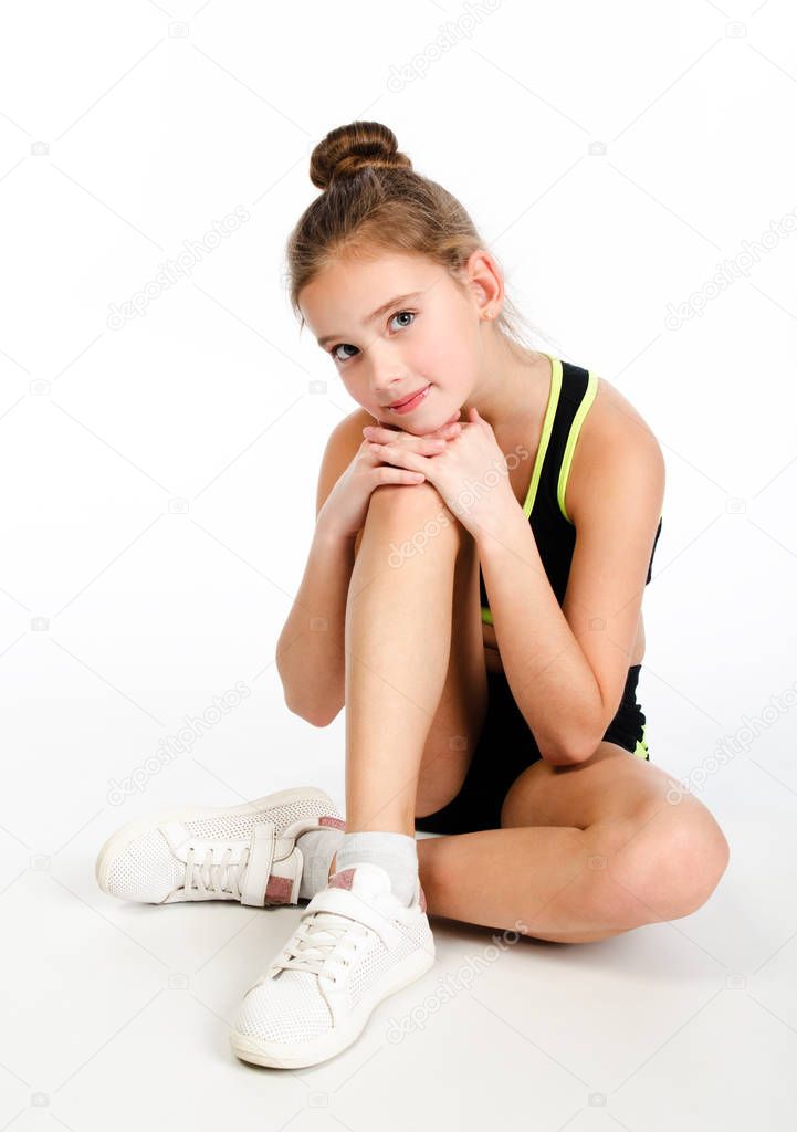 Gymnast smiling little girl child sitting on a floor isolated on