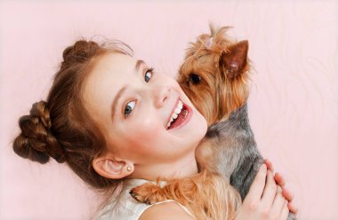 Sevimli, gülümseyen küçük kız liseli kız köpek Yorkshire Teriyeri 'ni tutuyor ve onunla oynuyor. 