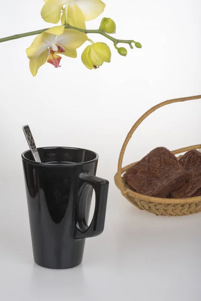 Csésze fekete kávé, csokoládé teasütemények és sárga orchidea — Stock Fotó