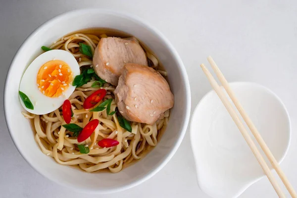 Ramen noodle çorba tabağı ile yarı haşlanmış yumurta, sebze, hafif bir arka plan üzerinde ahşap yemek çubukları. Üstten Görünüm.