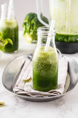 Beyaz masadaki malzemelerle harmanlanmış yeşil smoothie..