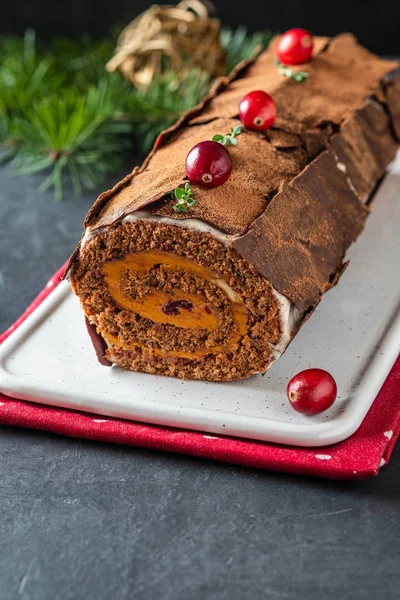 Buche de Noel. Traditional Christmas dessert, Christmas yule log cake with chocolate cream, cranberry. On stone gray background with Christmas tree branches. — Stock Photo, Image