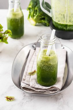 Beyaz masadaki malzemelerle harmanlanmış yeşil smoothie..