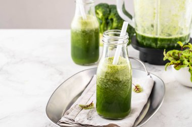 Beyaz masadaki malzemelerle harmanlanmış yeşil smoothie..