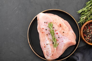 Baharat ve otlar ile siyah kesme tahtası üzerinde çiğ hindi fileto. Pişirme malzemeleri. Doğal sağlıklı gıda kavramı. Metin için yer ile üstten görünüm