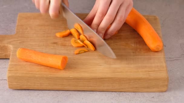 Mulher corta cenouras para sopa. Mãos que cortam cenouras em uma tábua de corte. Jovem mulher cortando legumes na cozinha. Movimento lento. Vista lateral . — Vídeo de Stock