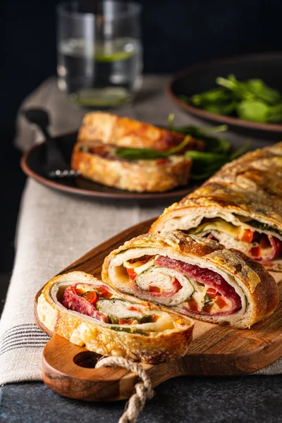 Geleneksel İtalyan Stromboli peyniri, salam, kırmızı biber ve ıspanakla doldurulmuş. Fotoğraf koyu renkli..