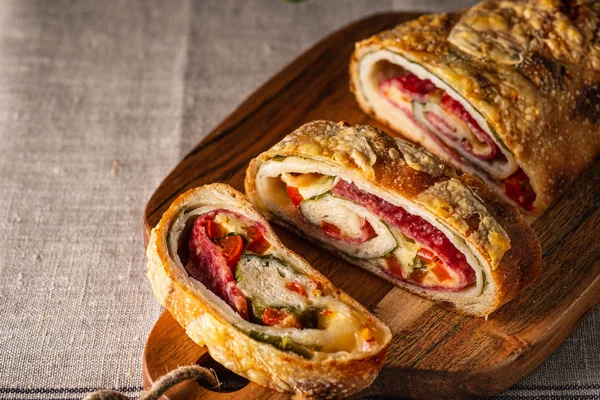 Traditional Italian Stromboli stuffed with cheese, salami, red pepper and spinach. Photo in a dark style. — Stock Photo, Image