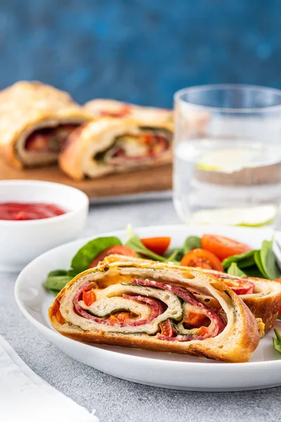 Italian food Pizza roll stromboli with cheese, salami, spinach and red pepper a light background. — Stock Photo, Image