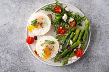 Toasts with asparagus and a fried egg on a white plate, top view, grey background.