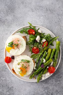 Toasts with asparagus and a fried egg on a white plate, top view, grey background.