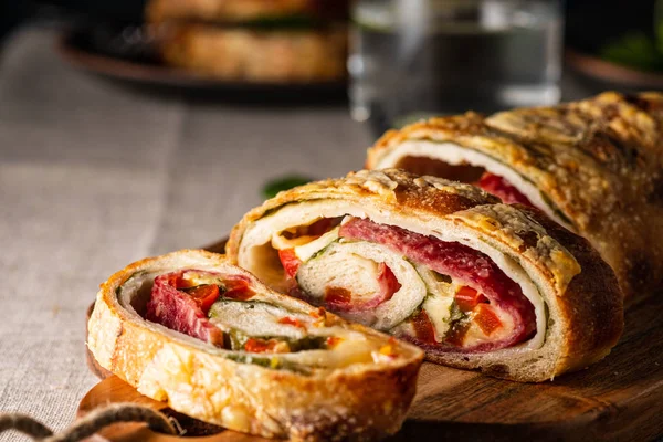 Tradicional Stromboli italiano relleno de queso, salami, pimiento rojo y espinacas. Foto en un estilo oscuro . — Foto de Stock