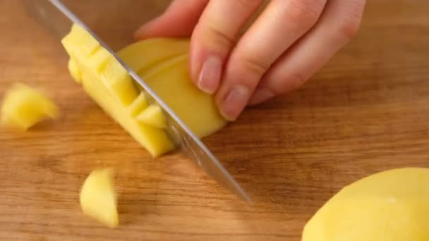 Γυναικεία χέρια κόβουν ωμές πατάτες με μαχαίρι σε ξύλινη σανίδα. Κόβω πατάτες. Παρασκευή σούπας. — Αρχείο Βίντεο