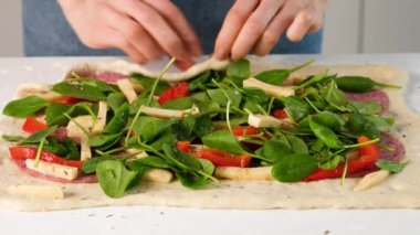 İtalyan yemeği yapan kadın eller peynirli, mozzarellalı, salamlı, domatesli, ıspanaklı ve kırmızı biberli pizza..