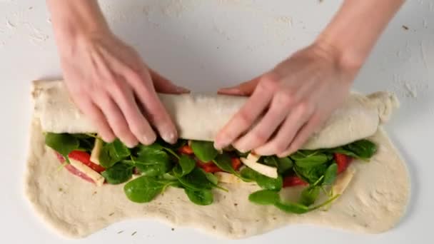 Manos femeninas haciendo comida italiana Pizza roll stromboli con queso, mozzarella, salami, tomates, espinacas y pimiento rojo un fondo claro . — Vídeos de Stock