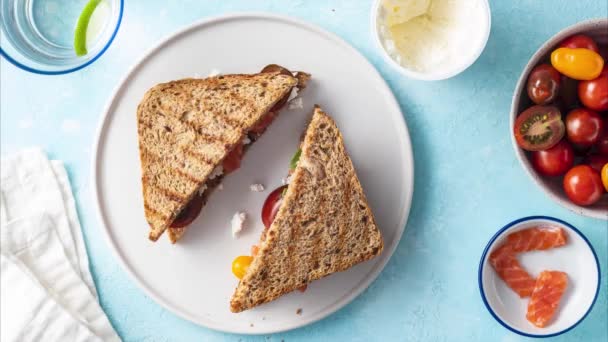 Sandwich with cheese, cottage cheese, tomatoes, salmon, spinach, bread, the process of making sandwiches with various fillings on a blue background, top view, 4k, stop motion animation — Stock Video