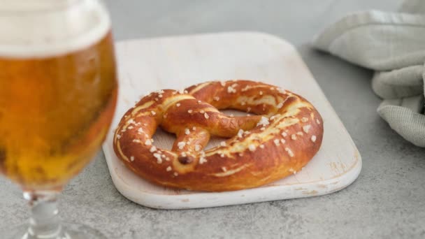 Oktoberfest food menu, soft pretzels and beer on a wooden board and white background. Beer is poured. Misted glass with beer. Female hands take britzel.