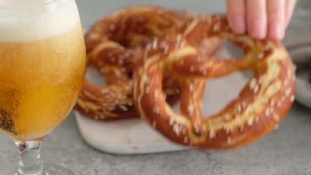 Menù dell'Oktoberfest, pretzel morbidi e birra su una tavola di legno e sfondo bianco. La birra è versata. Bicchiere Misted con birra. Mani femminili prendere britzel . — Video Stock