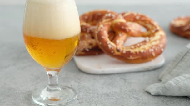 Menú de comida Oktoberfest, pretzels suaves y cerveza sobre una tabla de madera y fondo blanco. La cerveza se vierte. Vidrio nublado con cerveza. Las manos femeninas toman britzel . — Vídeo de stock