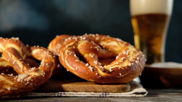 Oktoberfest food menu, soft pretzels and beer on wooden background. Beer is being poured. Misted glass with beer. Slow motion. — Stock Video