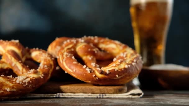 Oktoberfest menu de comida, pretzels macios e cerveja em fundo de madeira. A cerveja está a ser derramada. Copo misturado com cerveja. Movimento lento . — Vídeo de Stock