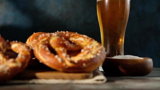 Oktoberfest menu de comida, pretzels macios e cerveja em fundo de madeira. A cerveja está a ser derramada. Copo misturado com cerveja. Movimento lento . — Vídeo de Stock