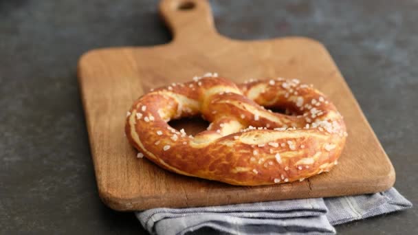 Oktoberfest menu de comida, pretzels macios e cerveja em uma tábua de madeira e fundo escuro. A cerveja é derramada. Copo misturado com cerveja. Mãos femininas tomar britzel . — Vídeo de Stock