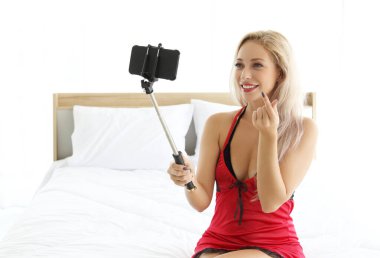 Güzel bir kadın yatak odasında cep telefonu kullanıyor ve selfie çekiyor.