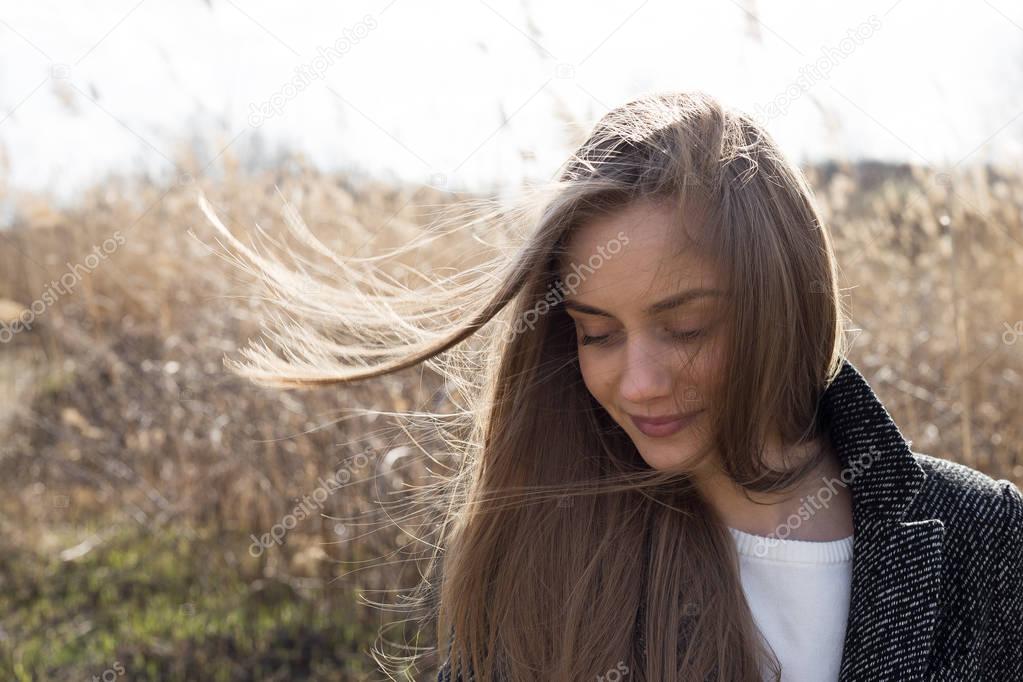 Beautiful young woman dressed in a woolen coat looks sideways and smiling. Autumn. Outdoor. Headshot.