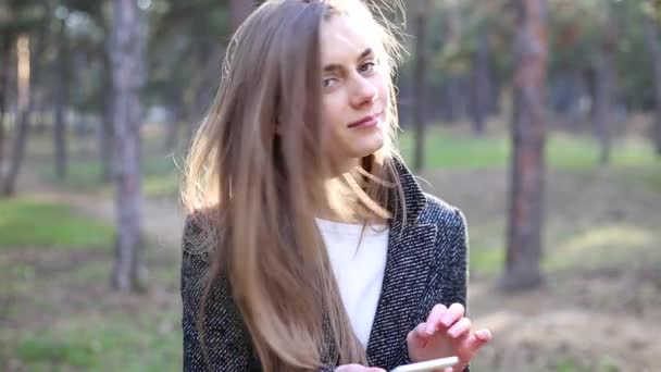 Menina virou-se, olhou para a câmera, sorriu e continuou a procurar algo no telefone — Vídeo de Stock