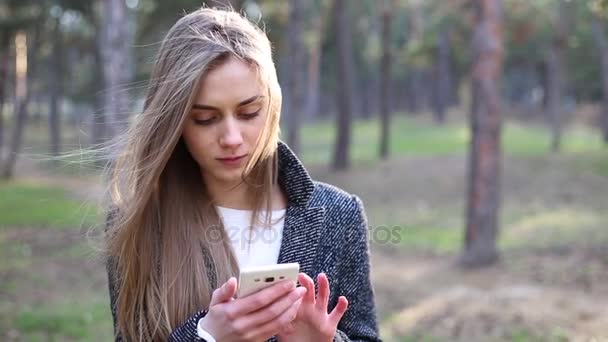 Giovane bella donna con i capelli biondi comporre un numero di telefono e dopo aver parlato sul cellulare nel parco — Video Stock