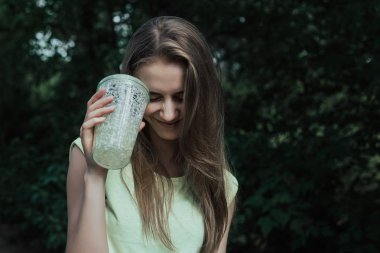 Young european woman with long blond hair stands in park and smiling with closes eyes.