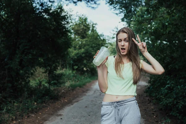 Kız barış onun elini imzalamak ve göz kırpıyor yapar. Kadın içki ile bardak fincan ile parklar yolda duruyor. Orta atış.