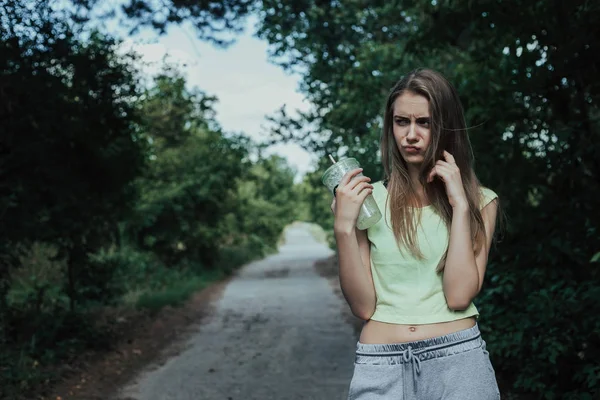 Joven deportista europeo chica con cuerpo atlético se para en parques de carretera con vaso en la mano . — Foto de Stock