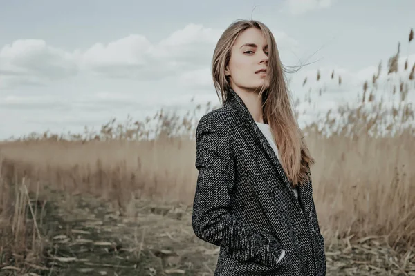 Mooie jonge vrouw gekleed in wollen jas poseren op camera op lisdodde achtergrond — Stockfoto