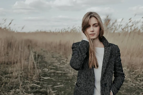 Красивая молодая женщина, одетая в шерстяное пальто, позирует перед камерой на фоне пули. Модель смотрит в камеру. Осень . — стоковое фото
