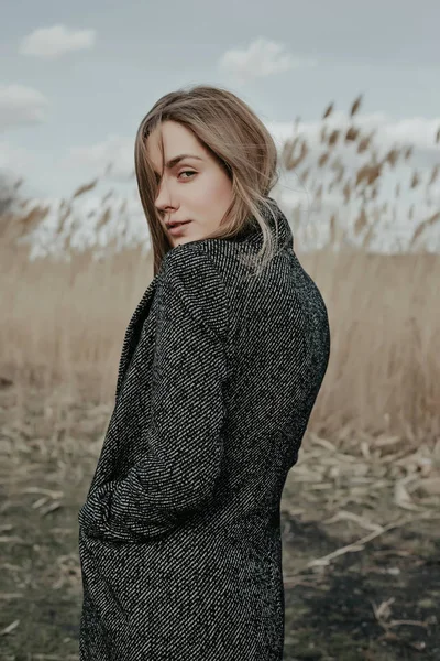 Woman in wool coat standing on a bulrush background.