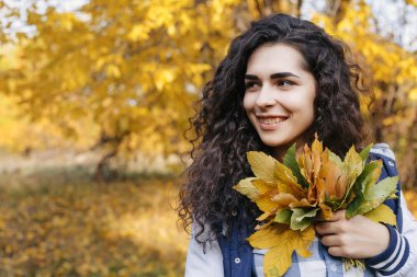 Sonbahar parkta duran ve yaprakları el avuç içinde tutan genç model