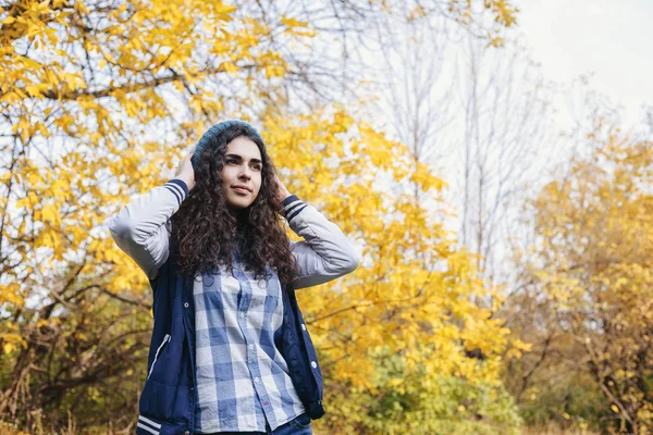Kız sonbahar ormanda ayakta ve şapka düzeltiyor