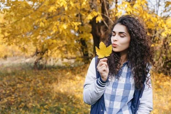 Piękna romantyczna dziewczyna stojąc w jesienny park i trzymając w ręku jeden jesień żółty liść i całować go — Zdjęcie stockowe